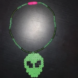 Handgjord Alien Choker - Handgjord alien choker/halsband. Gjort av glaspärlor och går att öppna och stänga. Alien är av pärlplatta. Halsbandet är stretchigt. Kan även göras i andra färgen och mptiv än just grön alien. Skickas mot fraktskostnad.