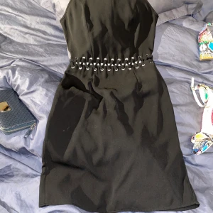 Svart mini-klänning  - Material: fint polyester, dvs ingen stretch. Färg: svart. Strl: 34 Märke: Ginatricot. Gömd lång dragkedja i söm på ryggen, fin detalj i mitten där hud visas. 