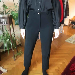  - svarta byxor i stretchigt material. hög midja och raka ben, fina detaljer med dragkedjor på framfickorna. uppskattningsvis storlek 38