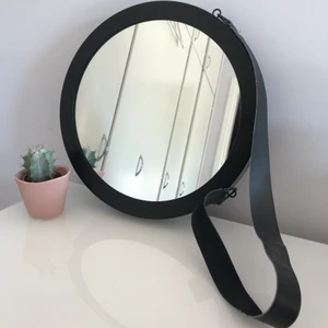 Rund väggspegel - En rund väggspegel med ram i svart metall. Spegeln har två öglor med ett svart läderband för upphängning. Diameter 30cm. 