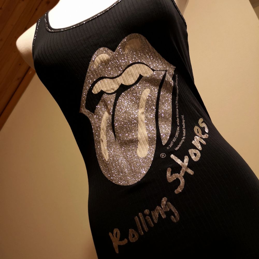 Svart långt linne med Rolling Stones-tryck i silvrigt glitter som snor snyggt åt kring kroppen. Helt oanvänd, som ny! . Toppar.