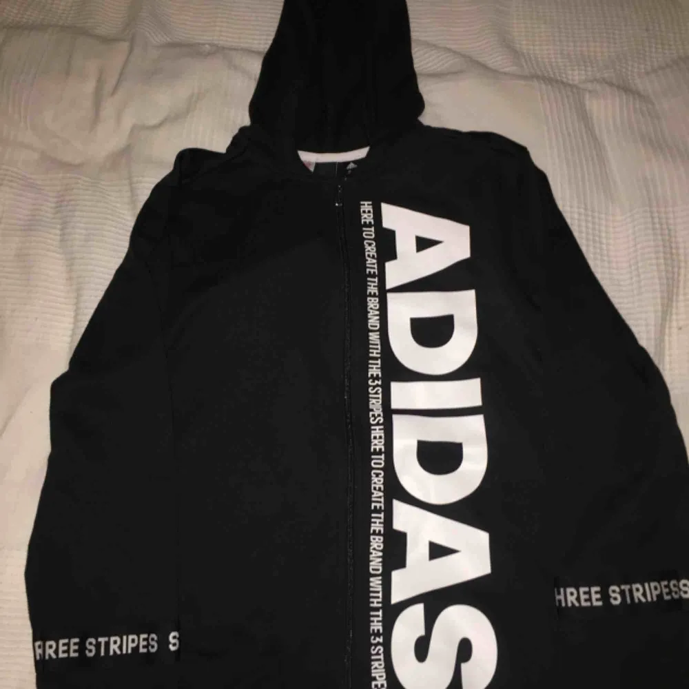 En Svart Adidas hoodie med dragkedja och Adidas text på vänstra sidan. Väldigt bekväm. Köpte orginält den för 500kr.. Hoodies.