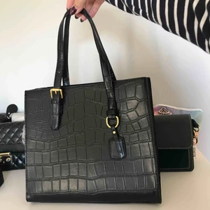Ny svart handväska med krokodilmönster - L: 26cm  B:21cm D:15cm . Vegansk svart väska med korkodilmönster och guldiga detaljer. Medföljer ett mörkbrunt axelband som tillhör väskan. Aldrig använd pga för liten. Jättefin väska att använda till vardags. Exklusive frakt