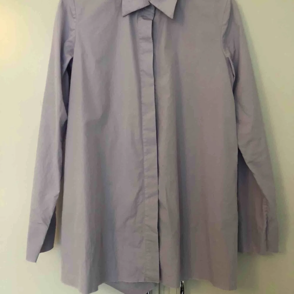 Syrenlila skjorta från COS i storlek 36. Skjortan är A-linjeformad så den är större nertill och mer figursydd upptill. Aldrig använd av mig, endast tvättad en gång. Avklippta detaljer. I perfekt skick! Frakt 63kr/upphämtning Södermalm. Skjortor.