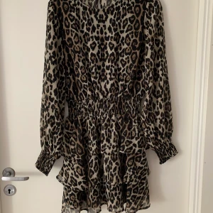 Klänning med leopardmönster - Klänning från ginatricot med volangkjol. Armarna är lite egenomskinliga, lite åt mesh hållet (se bild 3) Använd 1 gång, nyskick. Sitter fint på, passar xs också. Buda i kommentarerna. Slutsåld på hemsidan