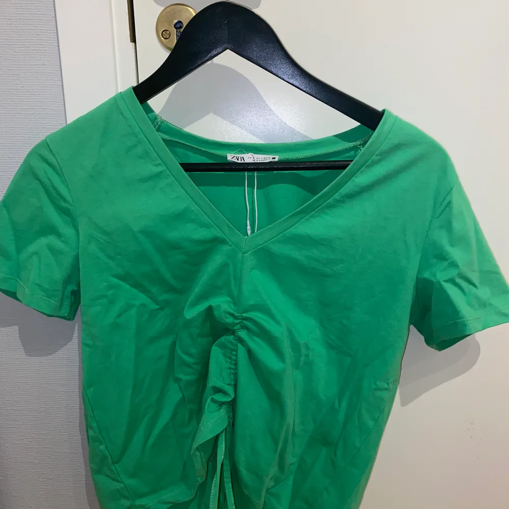 Grön v-ringad tshirt med ”zip up”. Helt nu och oanvänd. Prislapp kvar. Från Zara tidigare. Jättebra skick. Frakt tillkommer. Toppar.
