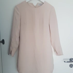 J lindeberg klänning 36 - J lindeberg klänning i fin ljusbeige/rosa färg. Rundade kanter nertill och snygga slitsar vid ärmslut. Klänningen har fastsydd/inbyggd underklänning så man ser inte igenom något alls   Storleken är 36 men är förkortad (uppsydd hos skräddare) så mer som 34