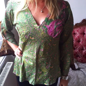  - Mycket fin sidenblus, 2 blusar i 1, man kan nämligen vända ut och in på den. Väldigt vackert mönster på båda sidor och väldigt vackra färger. Öppna armar med band och fin passform. Oanvänd! Hade gärna behållt den, men köpte den utan att prova och den passar tyvärr inte mig i storleken. Nypris: 300:-