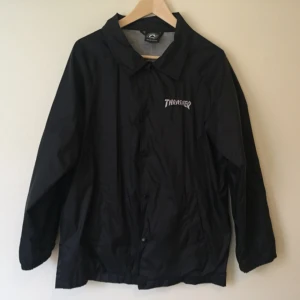  - Coach jacka från skateboard märket Thrasher. Storlek saknas, uppskattad till Medium herr (jag har S i dam, och den är snyggt oversized). Regntåligt material, grått foder. Två fickor på framsidan, och en inneficka. Använd enbart ett fåtal gånger.