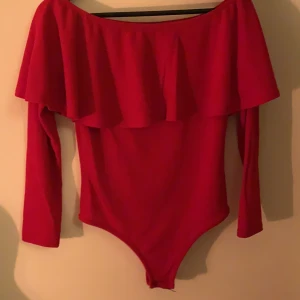 Röd body med volang - Jättefin body från Nelly i storlek S. En liten fläck på volangen som knappt syns från håll. string på baksidan