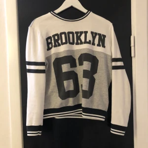 Tröja - En tröja som det står BROOKLYN och 63 på. Den är vit o går med några svarta streck.