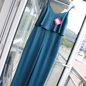 Underbar byxdress / jumpsuit  - Superfin byxdress från Even&Odd i härligt material och underbar, blå färg! Snygg modell, med dragkedja längs med ryggen som gör den figursydd. Löst hängande tyg från bysten och ner som ger ett fint fall. Köptes till ett bröllop men användes aldrig, storlekslappen sitter alltså kvar!  Fraktar mot betalning eller möts upp i GBG.  Storlek S.  96% polyester, 4% elastan.