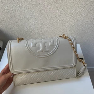 Tory burch väska - Säljer min fleming shoulder bag från Tory burch.  Mellanstor beige/benvit väska med Tory burch mönster, flätad axelrem med guldig kedja . Lite avskavt skinn.  Garanterad äkta, ej kvitto . Köp på raglady i Helsingborg. Skickas via postnord, går att spåras.