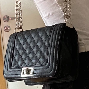 Svart handväska  - En väska som passar till allt, den kan användas som både axelremsväska och handväska då kedjan är justerbart och går att vika dubbelt. Den har två fack på insidan. Köpt på ur&penn  