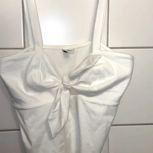 Vit topp med en rosett. St S - Helt oanvänd från nelly. Passar folk i xs också, för att den kan kjusteras med hur du knyter den.