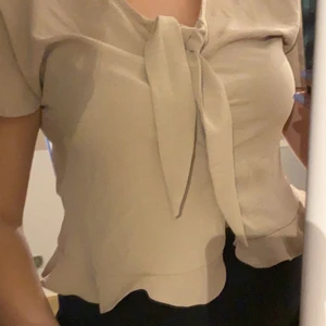 Volang topp stl 38 - Beige topp från vila med volanger, knytning och knappar på framsidan, knappt använd så i super fint skick 🙏🏻🙏🏻✨frakt tillkommer