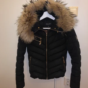 Hollies jacka strl 32 - Jag säljer min Hollies jacka som är använd 2 vintrar. Pälsen (äkta)  är helt perfekt och även jackan. Dock har en liten bit av dragkedjan gått av men det fungerar alldeles utmärkt. (Inget märkbart) Jag köpte den för 4500kr men säljer för 750kr. Hör av er!