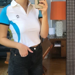 vit och blå topp storlek S - Säljer denna super snygga topp från ”Lotto”. Köpt second hand men har tyvärr knappt använts. Super bra skick. Jag tyckte om att vika upp den men på bild två ser du hur den ser ut nervikt. Öppen krage. Osäker på fraktkostnaden