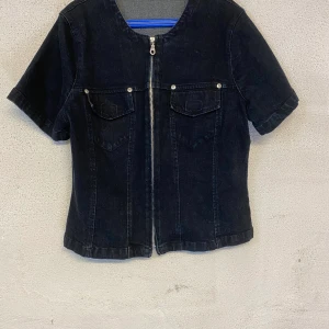 Vintage t-shorts i denim - Vintage t-shirt i jeans material. Dragkedja fram och även två bröstfickor. Färgen är mörkblå och den kommer i storlek S. Säljer för 50kr och köparen står för frakten.