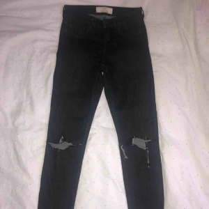  - Svarta jeans med slitningar på knäna. Helt ok skick med en liten fläck som syns på tredje bilden, inte helt säker på om den försvinner därav priset.
