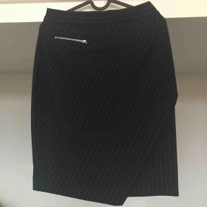  - Snygg kritstrecksrandig kjol med dekorativ dragkedja på framsidan. Kjolen går halvvägs ner på låren och sitter högt i midjan. Mörkt marinblå! 