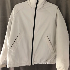 Vårjacka  -  En grå/beige jacka, kan användas som vindjacka. Muddar på armarna samt fickor på vardera sida med knappspänne 