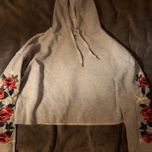 Kroppad hoodie. Str S - Grå kroppad hoodie med blomdetaljer på armarna. Ganska tunt material. 
