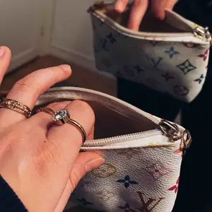 Fake Louis Vuitton väska där du får plats med mobil och plånbok. Perfekt att ha i handväskan och snygg. LV ”märken” i färg på en vit bakgrund. Köpare står för frakt. 