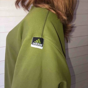  - En grön tröja i bomull från ADIDAS som är multifunktionell. På ena armen finns det ett adidas märke som en detalj. 