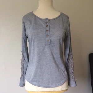  - Tröja med spetsdetaljerade ärmar och knapprad från halsringningen.    Frakt ingår ej, kan mötas upp i Stockholm