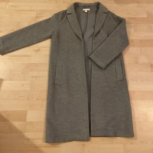 Grå lång kappa st. 34  - Säljer min stilrena ljusgråa långa kappa från HM. Köptes för något år sedan och är i nyskick och har därför NOLL defekter. Storlek 34. Nypris 799kr, mitt pris 300kr inklusive frakt, kan även mötas omkring hökarängen och då är priset 200 🥰