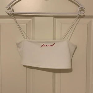 Vitt croppat linne från Nelly, storlek XS - Vitt croppat linne från Nelly, storlek XS med brodering av texten ”proud” i rött. Använt en gång så toppen är i mycket bra skick. 