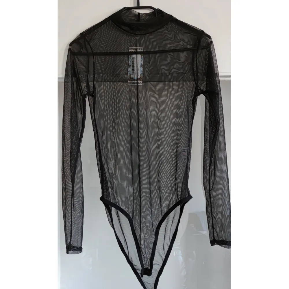 En långärmad svart mesh bodysuit som passar medium , storlek 40. Endast testad ,inte använd pga för liten och kort. Knappar för stägning i grenen.(för kort för 172cm lång kropp , passar kortare personer ). Toppar.