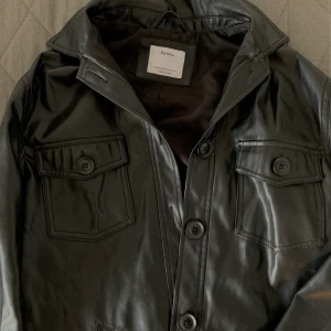 Skinnjacka  - Kappa/jacka i skinnmaterial från Bershka, funkar till allt nästan året runt, får plats att ha en tjock tröja under. Den går ungefär till höfterna och är i toppskick. Stl xs/s. Fraktar eller möts upp i Stockholm🤎🧸(på bilden ser den grå ut men den är helt svart) 