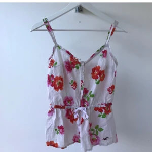 Linne från Hollister - Så fin blommig topp med knyte i midjan och fina detaljer från Hollister. Använd men i mycket fint skick! Storlek XS men passar även S!