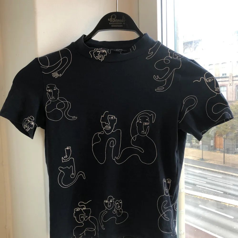 SÅ fin t-shirt från Monki med ett coolt mönster av ansiktsmotiv. Tröjan är marinblå. Halvpolo. Materialet är stretchigt vilket gör att tröjan sitter galet snyggt på. Har massor av snygga toppar uppe på min profil - kombinera gärna fraktpriset genom att köpa andra plagg. 🤩. T-shirts.