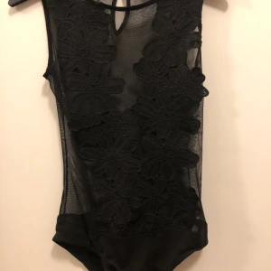 Blommig body - Superfin svart body i mesh men med mer täckande blommor över brösten. Passar bra på XS.