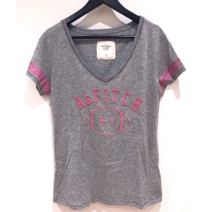  - T-shirt från Abercrombie&Fitch, grå med rosa detaljer och V-ringning. Passar S/M, även XS som lite lösare modell.