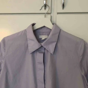  - Syrenlila skjorta från COS i storlek 36. Skjortan är A-linjeformad så den är större nertill och mer figursydd upptill. Aldrig använd av mig, endast tvättad en gång. Avklippta detaljer. I perfekt skick! Frakt 63kr/upphämtning Södermalm