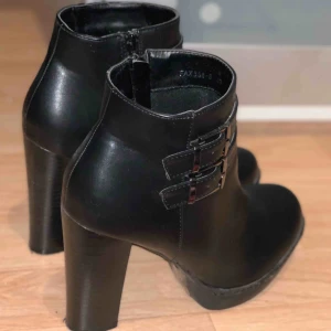  - Svarta ankelboots i konstläder. Detalj i form av spännen i sidan (utan funktion). Köpta utomlands, använda 2-3 ggr