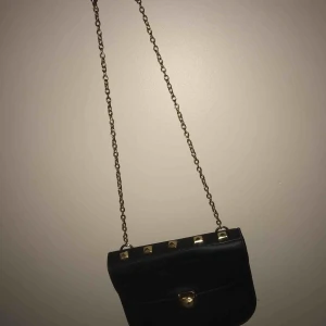  - En enkel axelbands väska. Svar med guldigt axelband och guldiga terapier som knäppen och uppepå väskan.