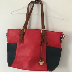 Röd & blå rymlig väska - Stor och rymlig Röd och mörkblå väska från Dudlin med bruna detaljer. Fin väska som är väldigt lite använd, perfekt för skola/jobb då den rymmer dator och böcker! 100kr utan frakt Möts i Sthlm eller fraktar