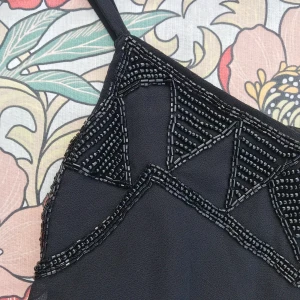 Pärlbroderad festklänning - Så fin festklänning!!! Har broderade svarta pärlor kring urringningen. Tunna axelband. Dold kedja i midjan. Tyvärr aldrig använd då den är för liten för mig 😭 Nypris 500:- 