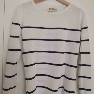  - Vit stickat tröja me blåa råder. Det finns en jätte liten orange fläck på armen. 