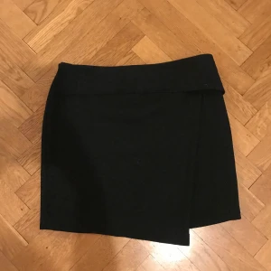 Svart kjol  - Svart omlottkjol med dragkedja och knäppning för band upptill. Mkt fint skick, använd 2ggr. 