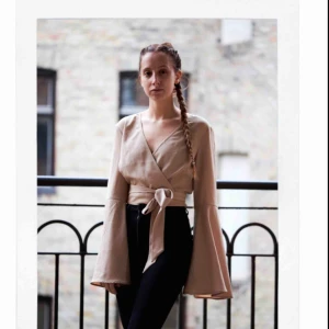  - HELT NYTT PLAGG FRÅN NA-KD. Jätte fin kortare blus/tröja/croptop med snyggt band som är fastsydd i toppen som man kan knyta till en fin rosett (bak eller fram). Beige färgad med snygga utsvängda armar och v-ringad. Kom gärna med eget pris 🌹