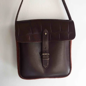 Väska  - Mörkbrun vintage handväska i måtten 19x21x5 cm. Väskan har ett litet innerfack med en dragkedja samt mocca liknande tyg på sidan. Axelbandet är lite slitet. Skriv till mig vid intresse eller om du har några frågor😄 Fraktkostnad tillkommer! 