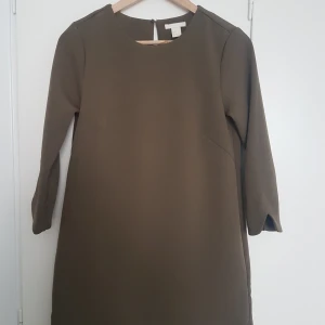 Mörkgrön klänning 34 - Mossgrön / mörkgrön klänning från h&m, strlk 34. Tjockt stadigt tyg! Har rundade kanter vid ärmslut och nedre kanten.