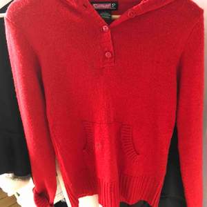 Långärmad röd tröja med luva och knappar, jätteskön att dra över något annat. Har en liten fläck på fickan fram, men syns inte mycket.