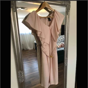  - Puderrosa klänning med volanger upptill och ett skärp med guldspånne i midjan.